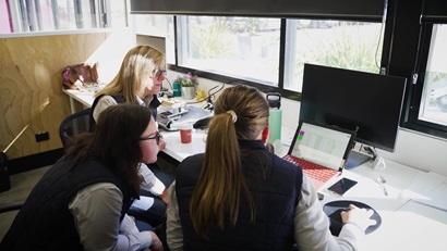 Bronwyn Darlington sitting at desk with students looking at a computer.