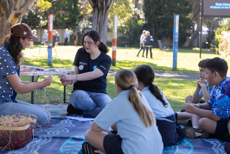 Students sitting on a picnic blanket outside in their school yard.