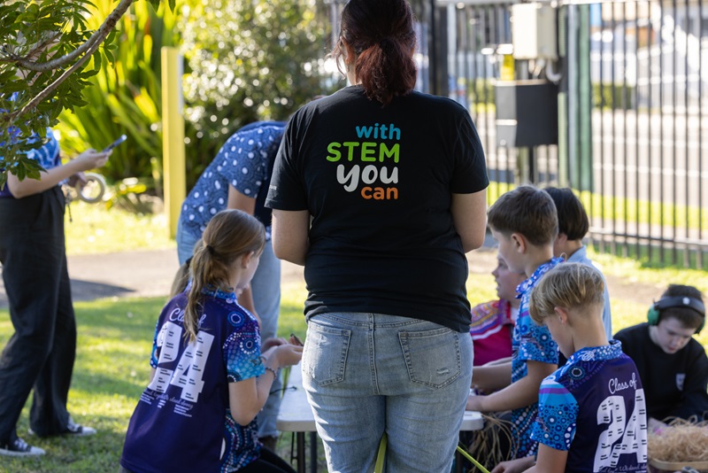 Students outside in their school yard. A teacher has her back to the camera, with the words 'with STEM you can' written on her t-shirt.
