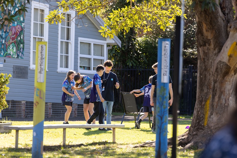 Students in blue uniforms walking and talking outside, in their school yard, in the sunshine.