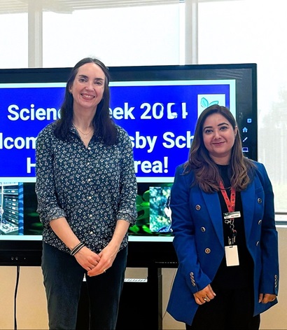 Two women standing in front of a screen and smiling into the camera