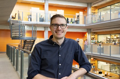 Dr David Riglar in a blue shirt wearing glasses sitting in an office space.