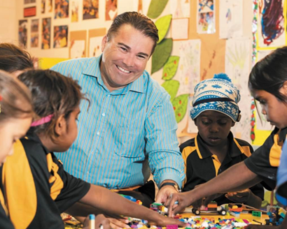 Shane Wilson smiles while surrounded by students playing with Lego