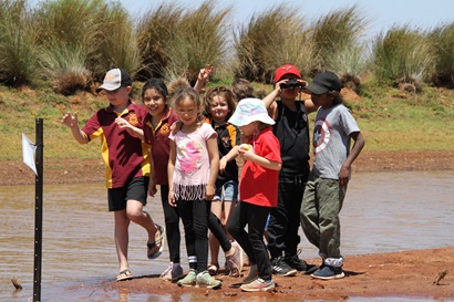 Leonora District High School students standing on a sandy bank near water. 
