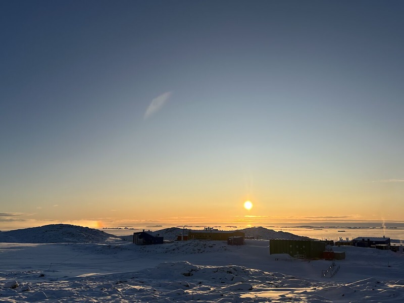 The sun sets over Casey station in Antarctica from afar. 