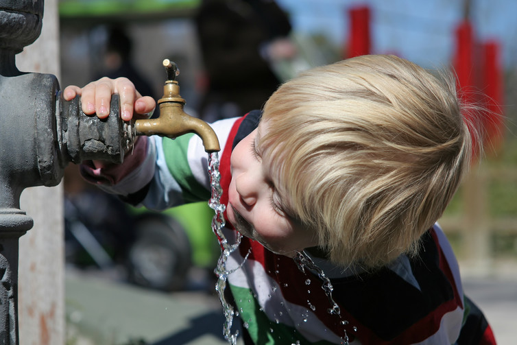 Young boy drinking water directly from a flowing garden tap. 