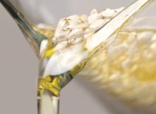A photo of oil and safflower seeds being poured out of a laboratory beaker.