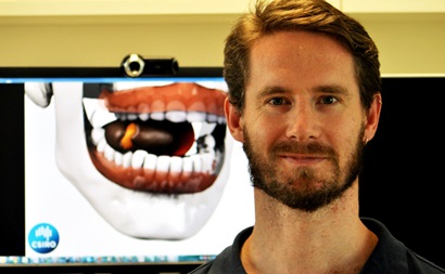 Dr Simon Harrison stands beside a monitor showing the virtual mouth model