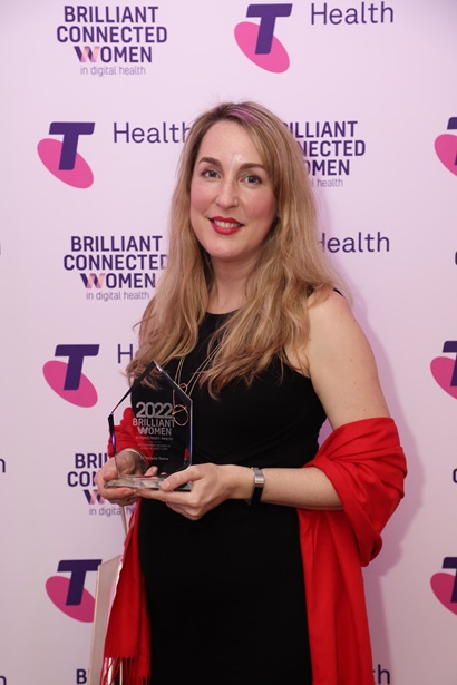 Image of Natalie Twine with her Telstra Health Brilliant Connected Women award standing in front of a Telstra Health banner