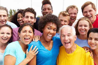 An image of a group of people taken outside. The group includes men and women, young and old as well as people from a diverse range of ethnicities. Everyone in the photo is smiling.