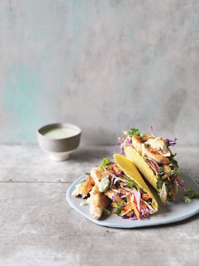 Two fish tacos served with salad on a plate sitting on a benchtop