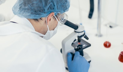 A person with looks into a microscope in a clinical laboratory setting 