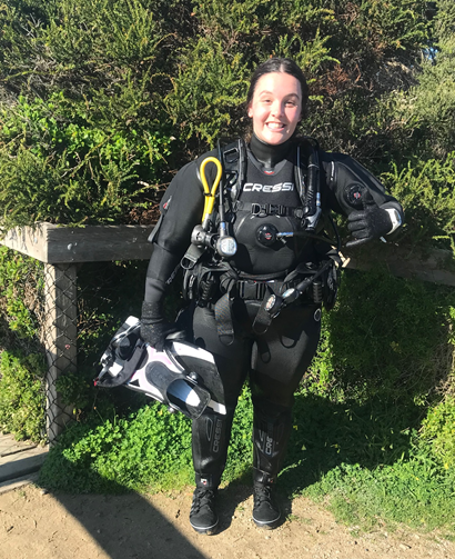 Picture of a woman dressed in diving gear. She is smiling at the camera.
