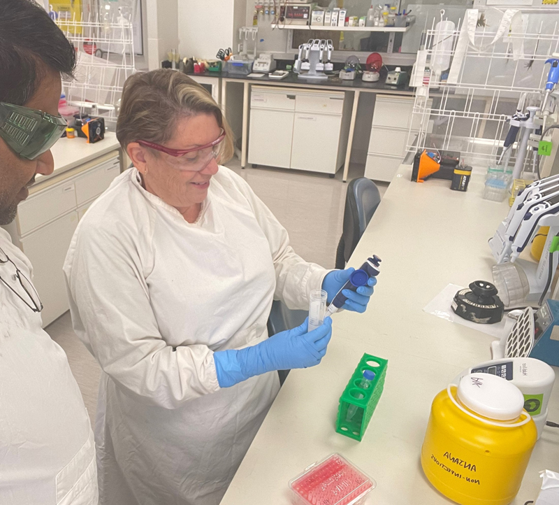 Woman wearing a white coat in a laboratory conducting an experiment, while another person in a white coat looks on. 