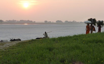 Grass on banks of the water at sunset with people standing on grass in India