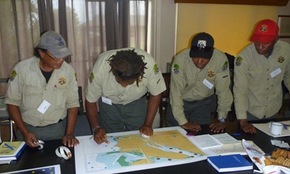 Four Indigenous rangers standing at a desk looking at a map