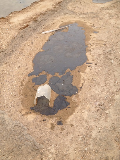 A tipped over plastic container with oil spilling out and pooling on the ground