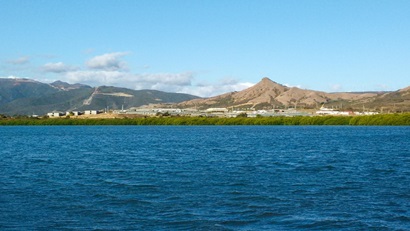 Stretch of blue water in front of mountainous landscape in the background, with buildings along the shoreline.