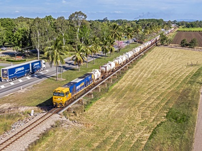 Aerial view, looking down on northbound Pacific National Queensland intermodal train on the iconic Ayr causeway with its line of Palm trees, as a B-double truck heads south along the Bruce Highway. Image by iStock