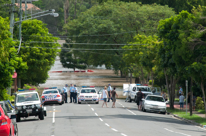 Flooded street with police car blocakde and people gathering to view the flood