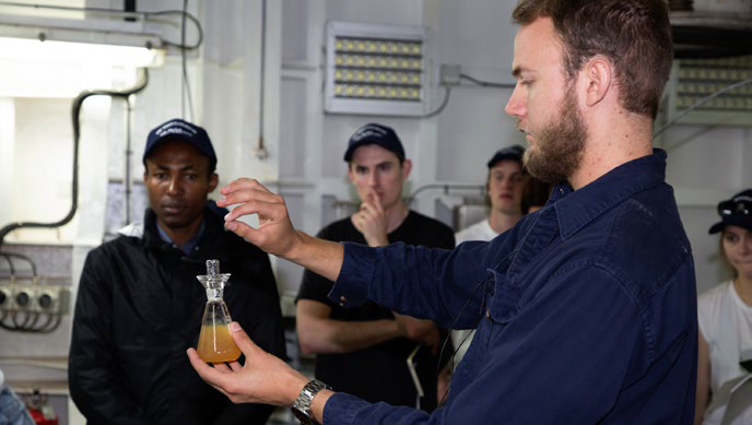 Scientist on board RV Investigator demonstrating a scientific procedure.