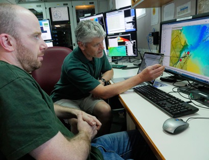 Two people working on a computer in the operations room on RV Investigator.