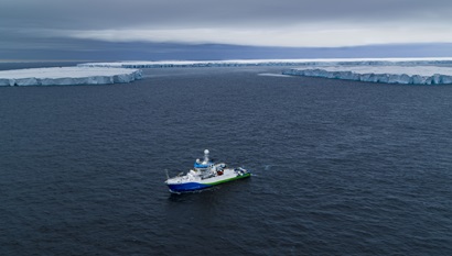 A ship photographed from above with icebergs in the background.