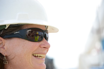 A close up of a woman in a hard hat smiling off camera.
