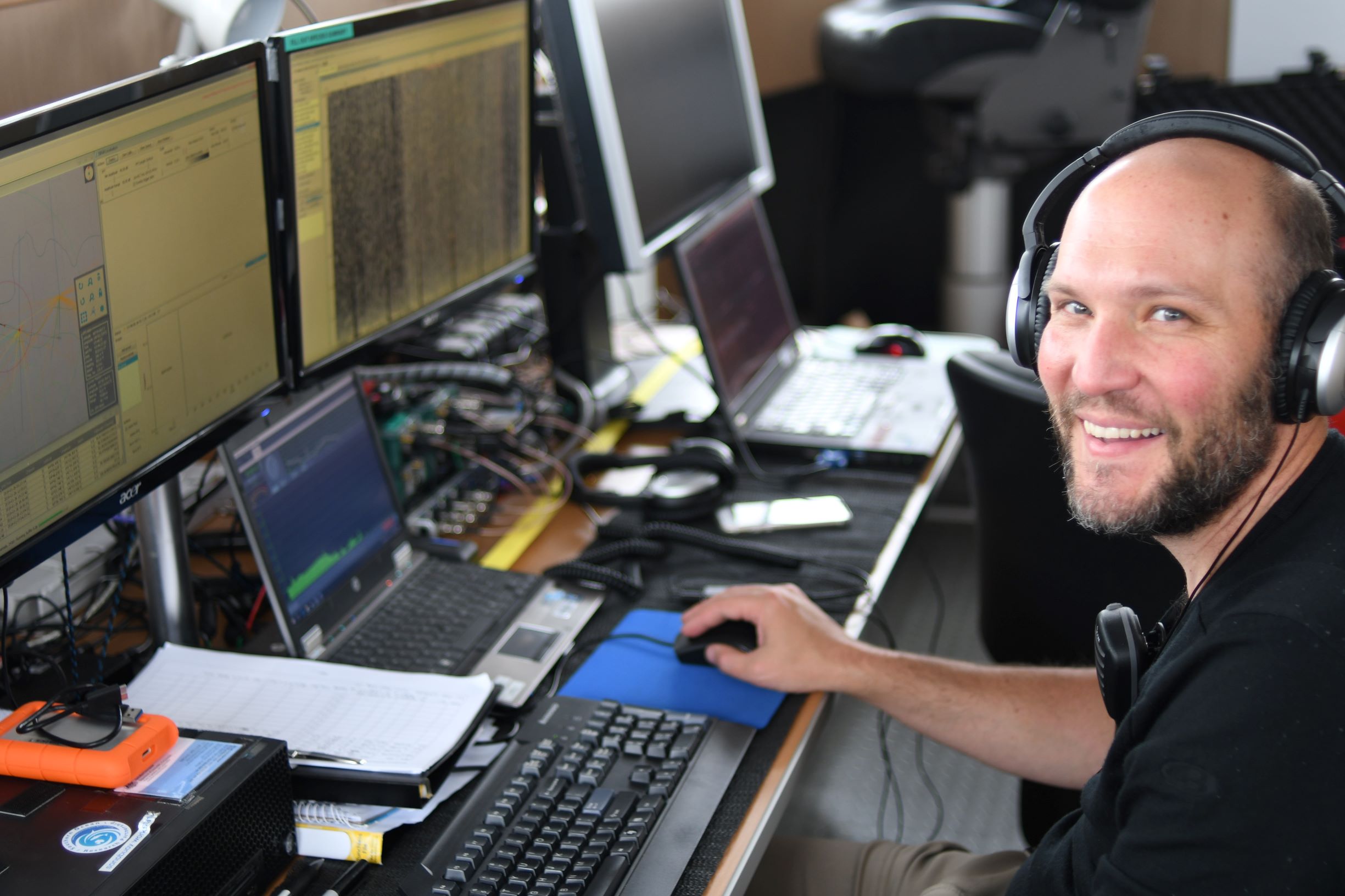 A man with headphones on sitting in front of a laptop.