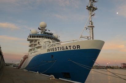 A large blue and white ship with Investigator written on the bow tied up alongside a wharf.