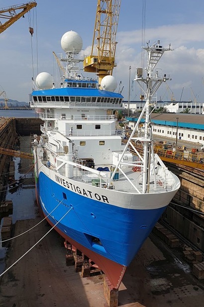 A large blue and white ship sits on blocks in a dock that has been emptied of water.