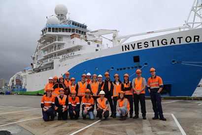 A group of people on a wharf in front of a blue and white ship.