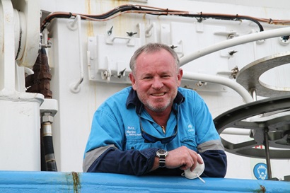 A photo of a person in a blue work shirt leaning on the railing of a ship.