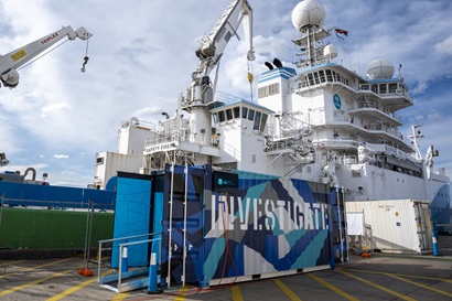 A container on a wharf next to a ship.