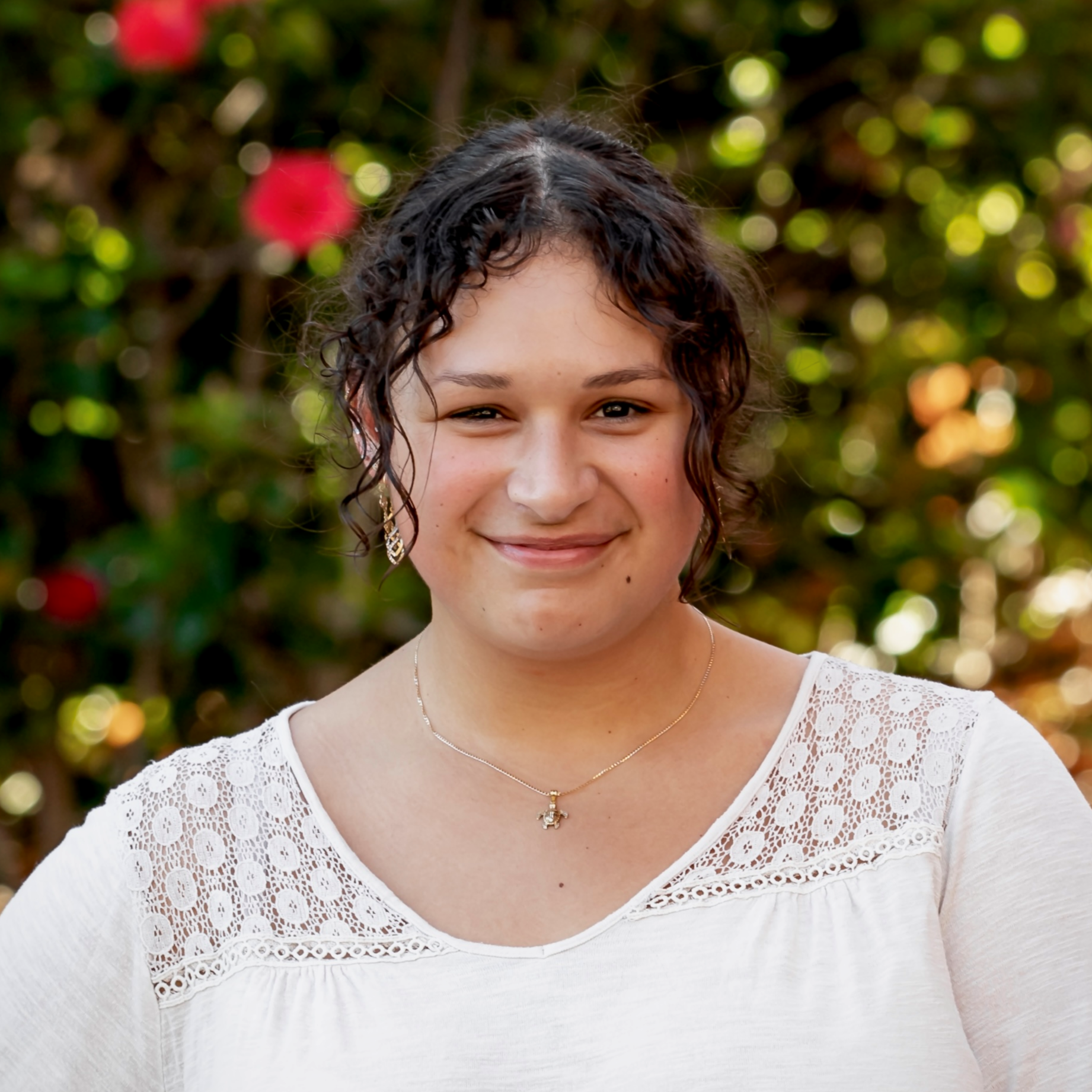 A profile photo of a person in a shite shirt standing in front of a tree with red flowers.