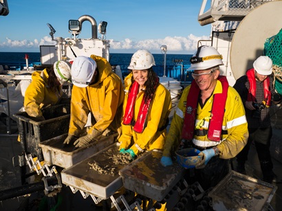 Four researchers standing and sorting through trays of mud, on the deck of the ship.