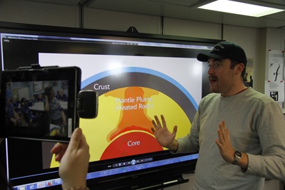A man gestures animatedly in front of a large monitor showing a colourful picture of a cross section of the Earth.