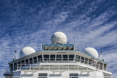 Three large white domes on top of the bridge of a ship with blue sky streaked with clouds in the background.