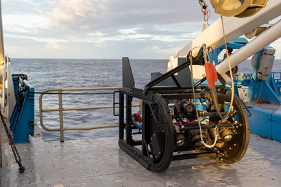 A large piece of scientific equipment that looks like a large toboggin sits on the deck of a ship.