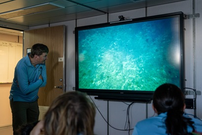 Three people watch a TV screen showing an underwater scene.