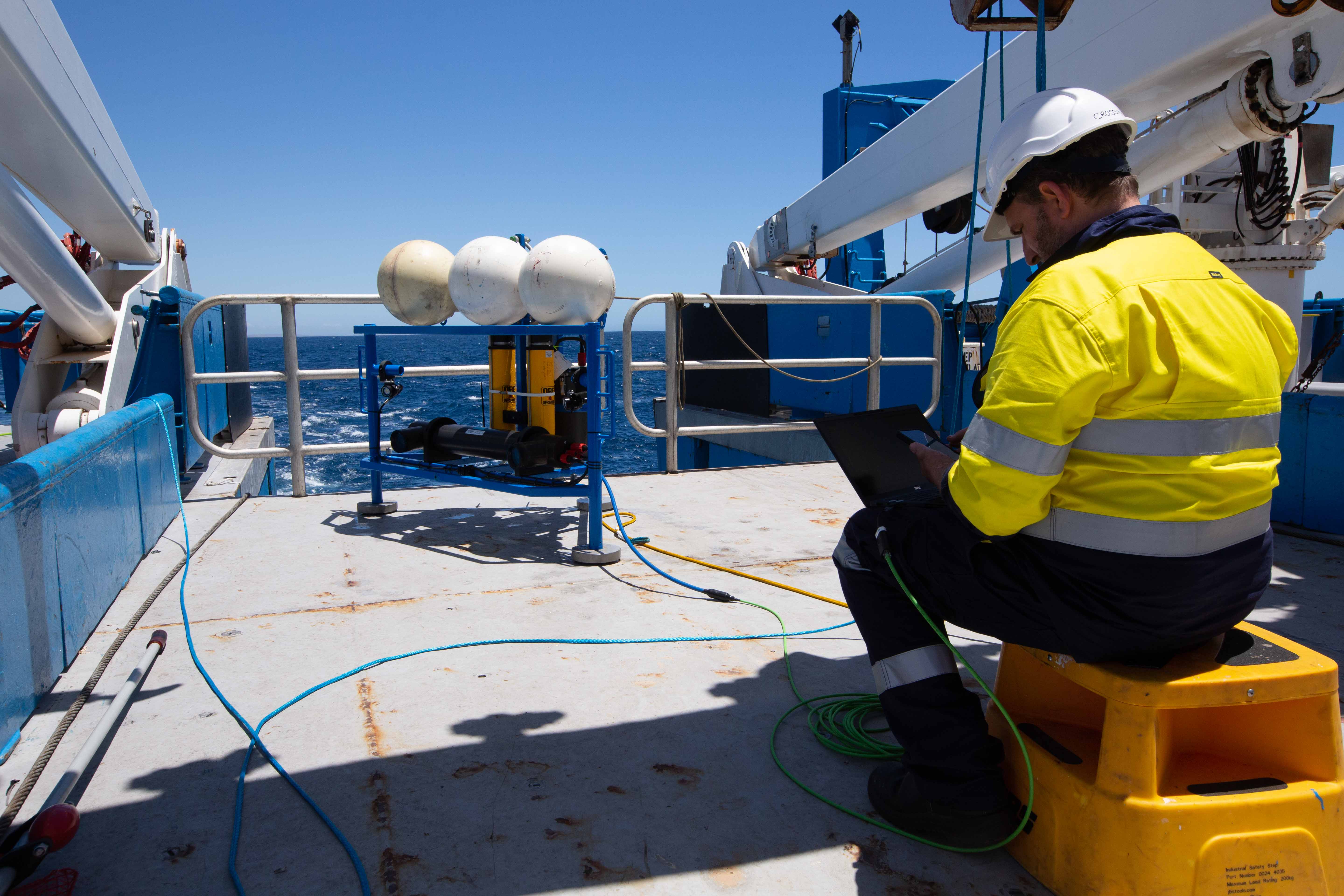 A person sitting on a small seat on the deck of a ship.