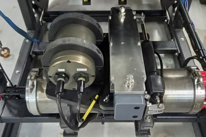 A shiny metal piece of scientific equipment mounted on the larger black frame of another piece of scientific equipment.