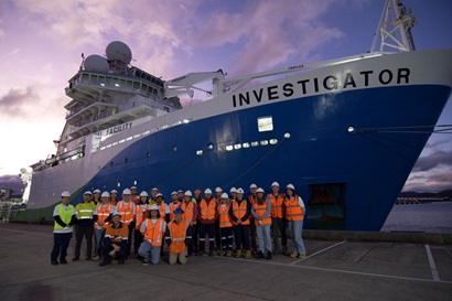 A group of people standing in front of a large blue and white ship at sunset.