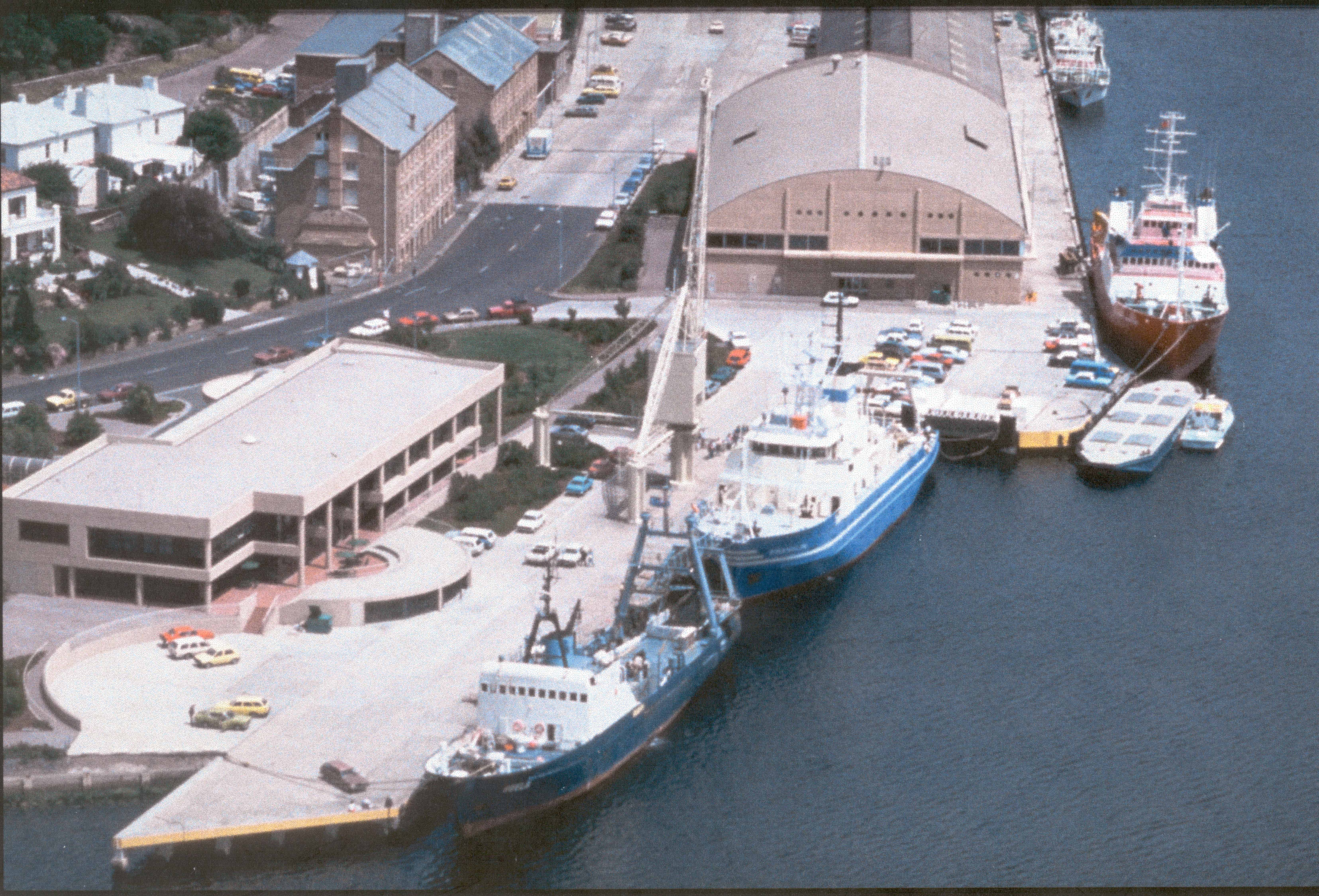 Three vessels alongside a wharf with various buildings next to the wharf.