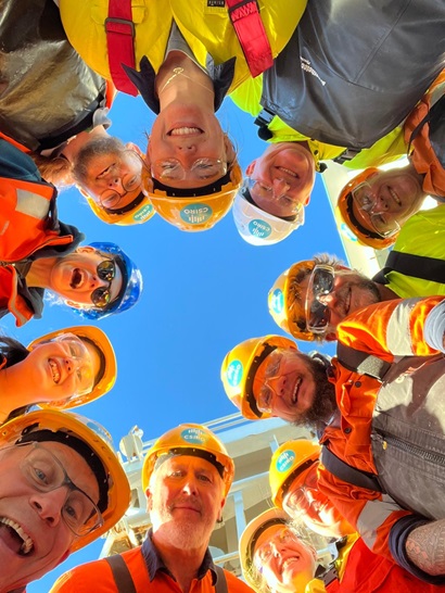 A group of people in hard hats and hi-vis vests staring down at the camera.