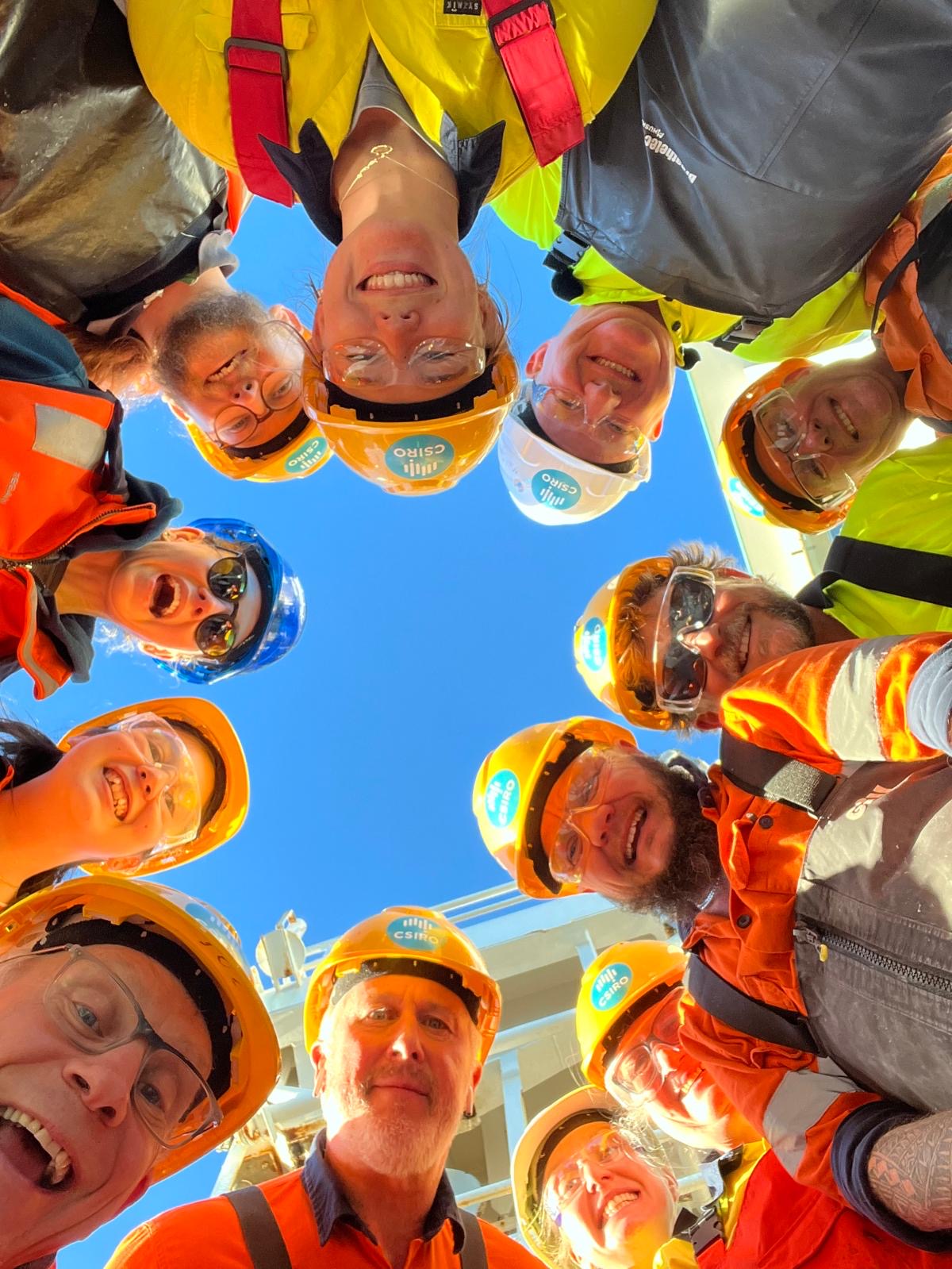 A group of people in hard hats and hi-vis vests staring down at the camera.
