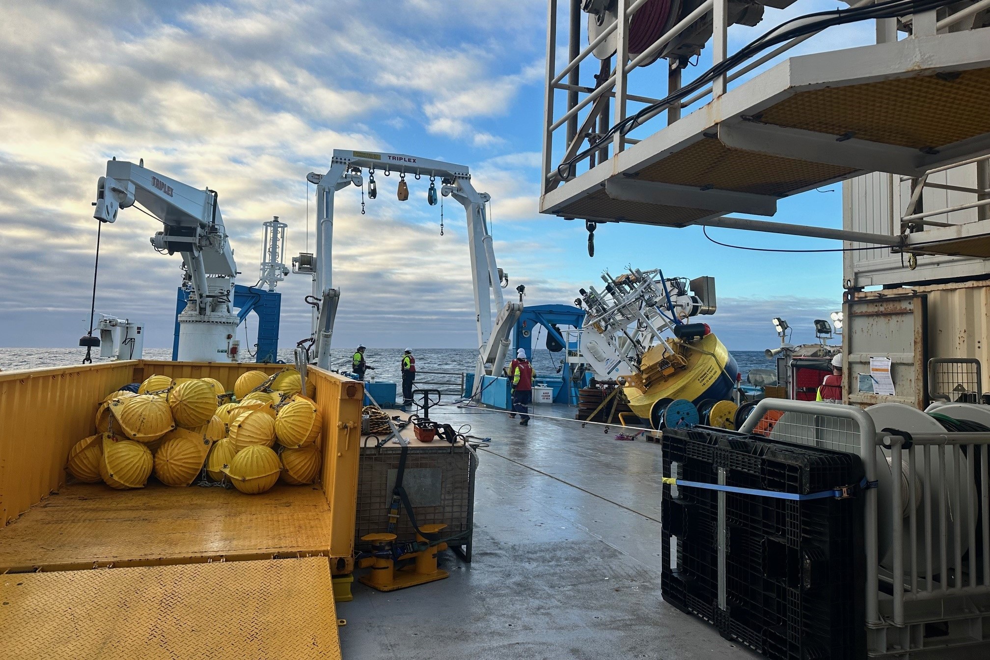 The back deck of a ship at sea with various scientific equipment stored on it.