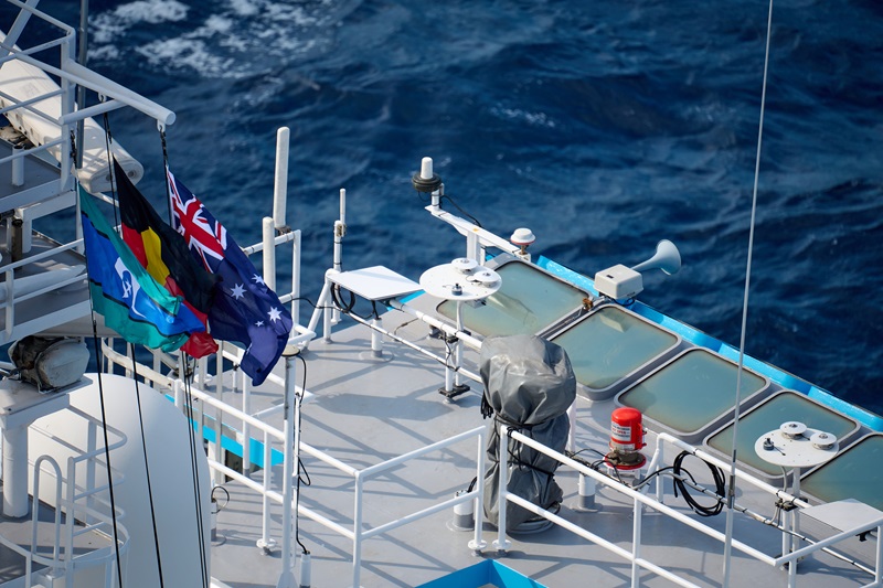 The Aboriginal flag, Torres Strait flag and Australian flag hoisted up the mast of ship.