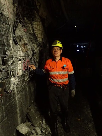 Man in high-vis and hard hard in an underground coal mine standing next to a wall protected by deformed wire mesh 