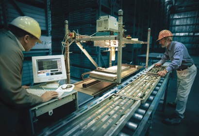 Two men in hard hats operating a prototype of hylogger machine to scan long trays of drilled rock.